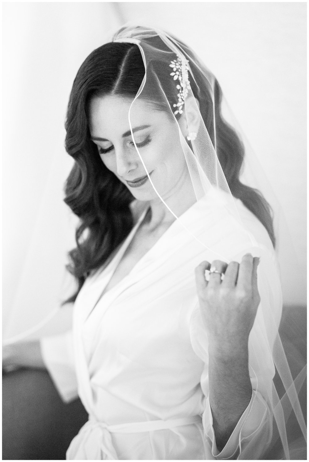black and white portrait of bride in white robe holding veil