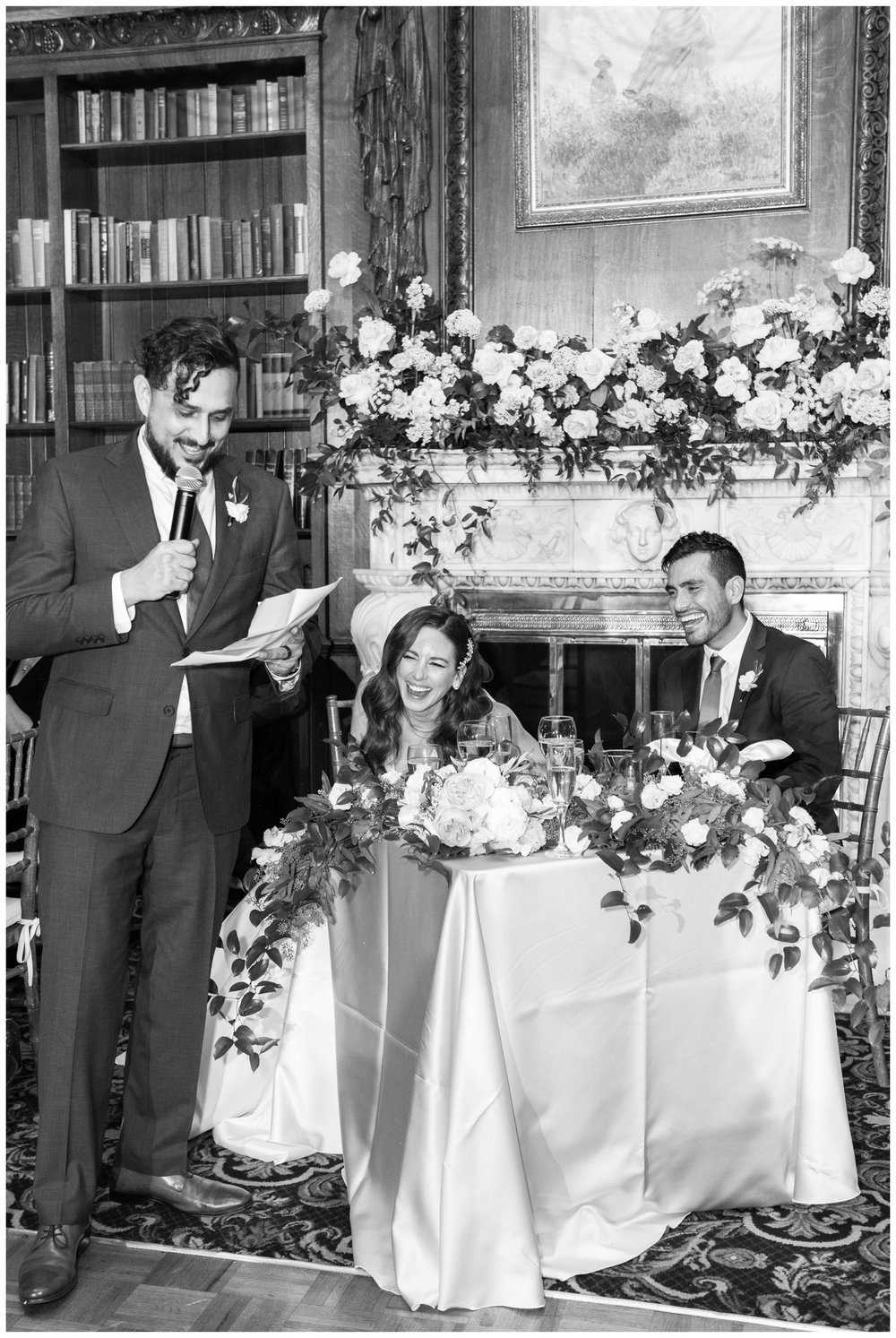 groomsman toasting with bride and groom sitting at floral sweetheart table