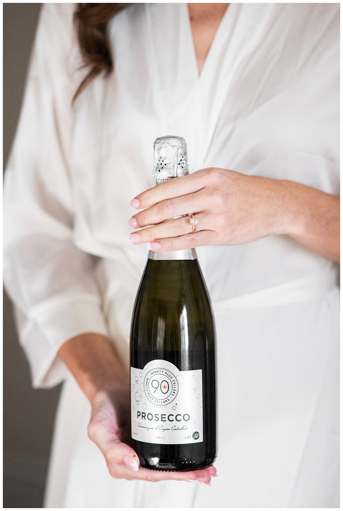 bride in white robe holding champagne bottle