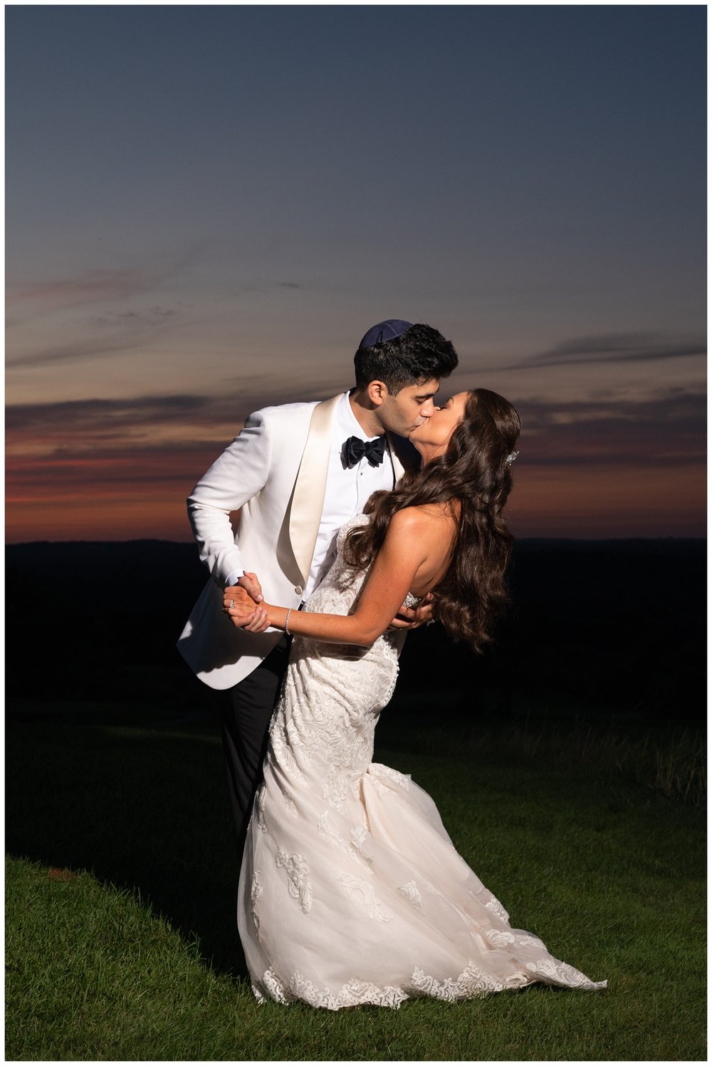 bride and groom standing on golf course kissing for night time wedding portrait