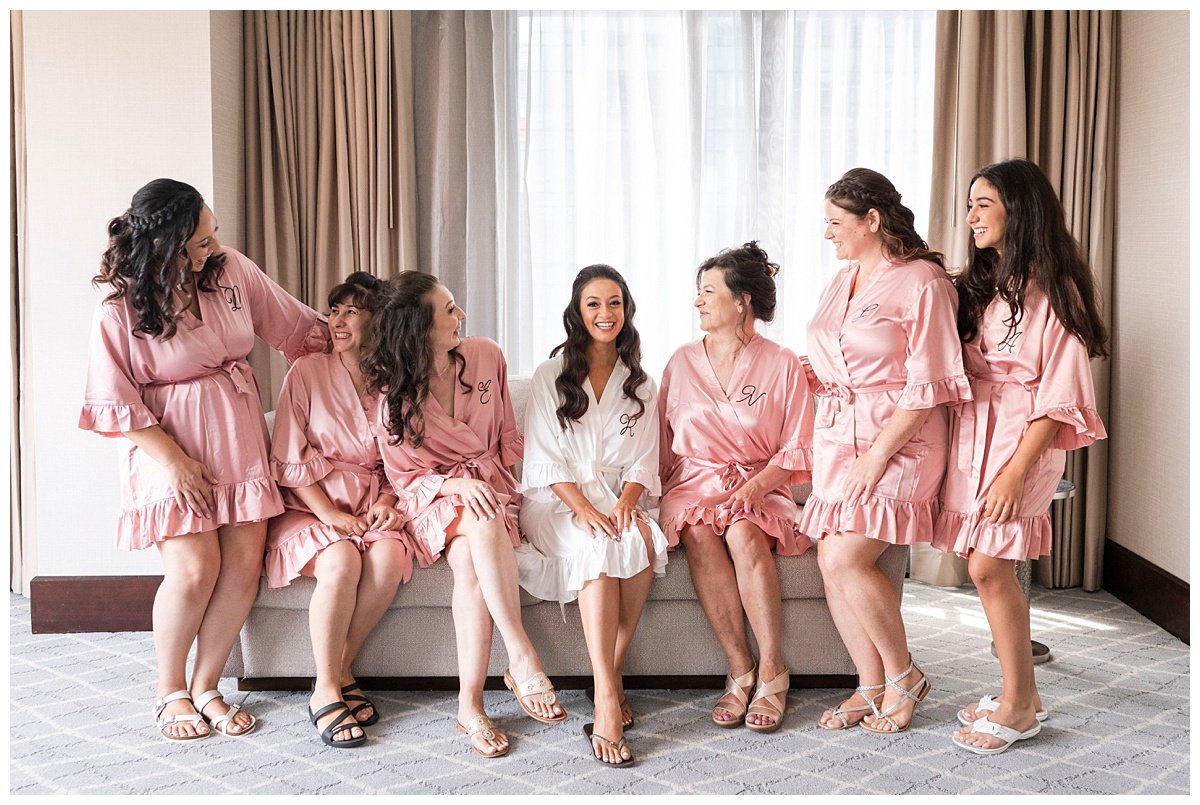 bride sitting with bridesmaids in pink robes laughing