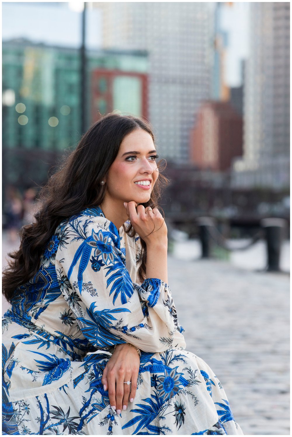 bride in navy and cream floral dress sitting at Boston Seaport with hand on chin