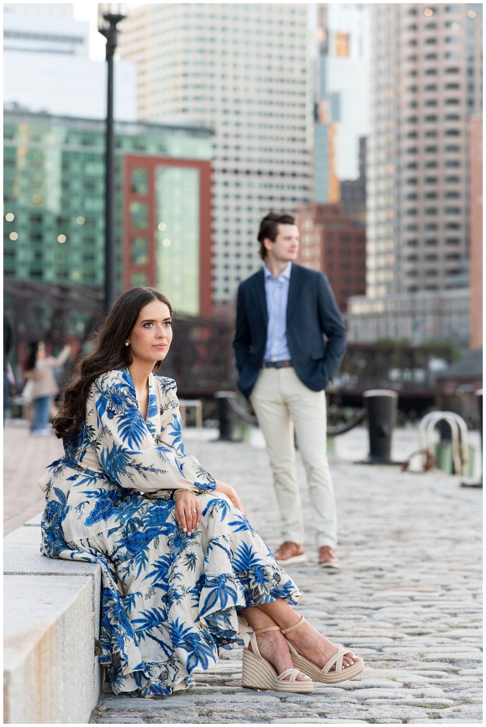 bride sitting at Boston Seaport with groom standing and looking over shoulder