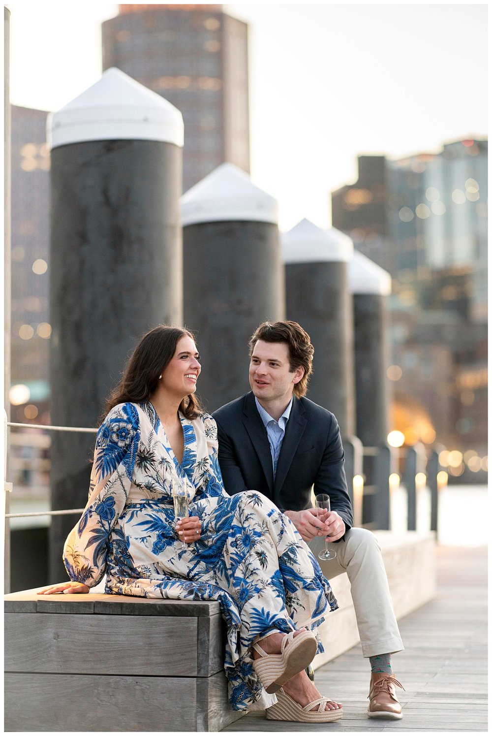 Boston Seaport engagement session champagne toast with couple sitting by water