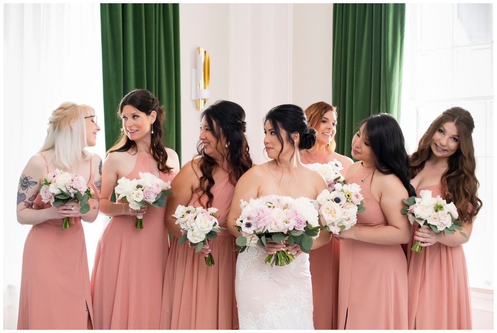 bride and bridesmaids in blush dresses laughing and holding bouquets