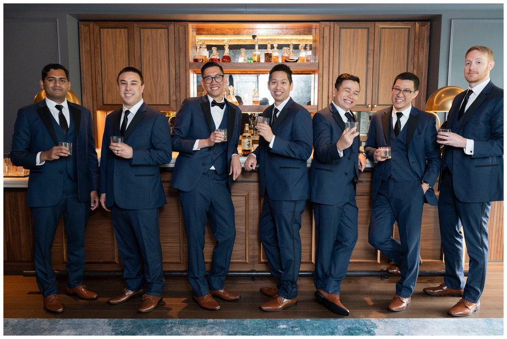 groomsmen and groom in navy tuxes toasting