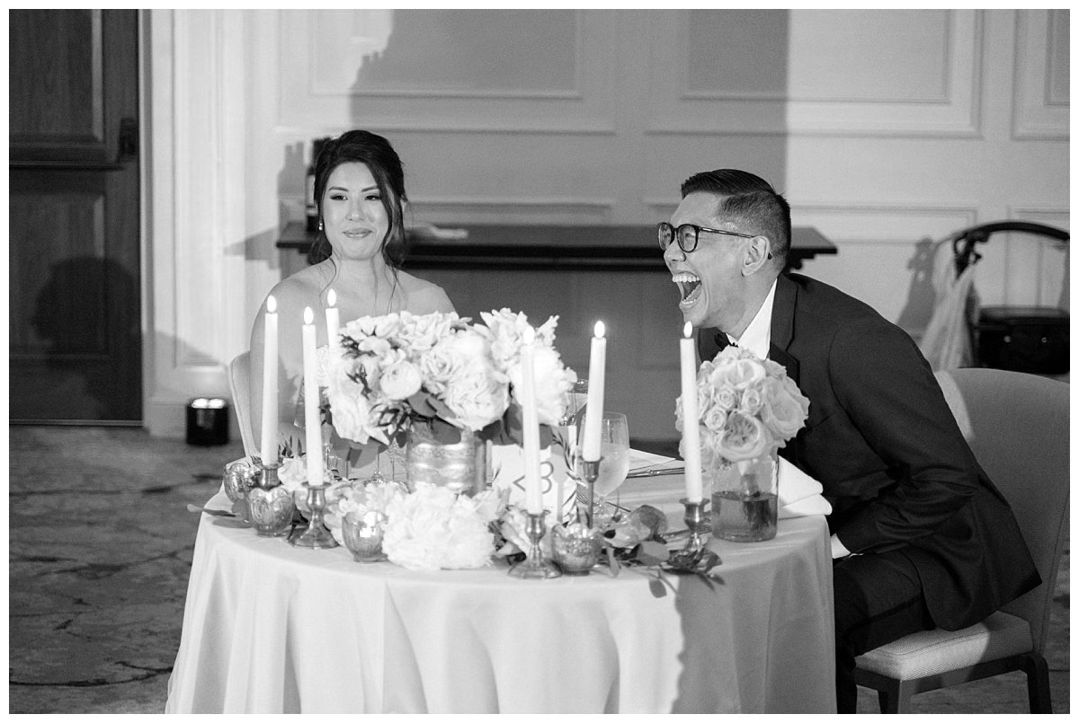 bride and groom laughing sitting at sweetheart table inside The Newbury Hotel wedding reception
