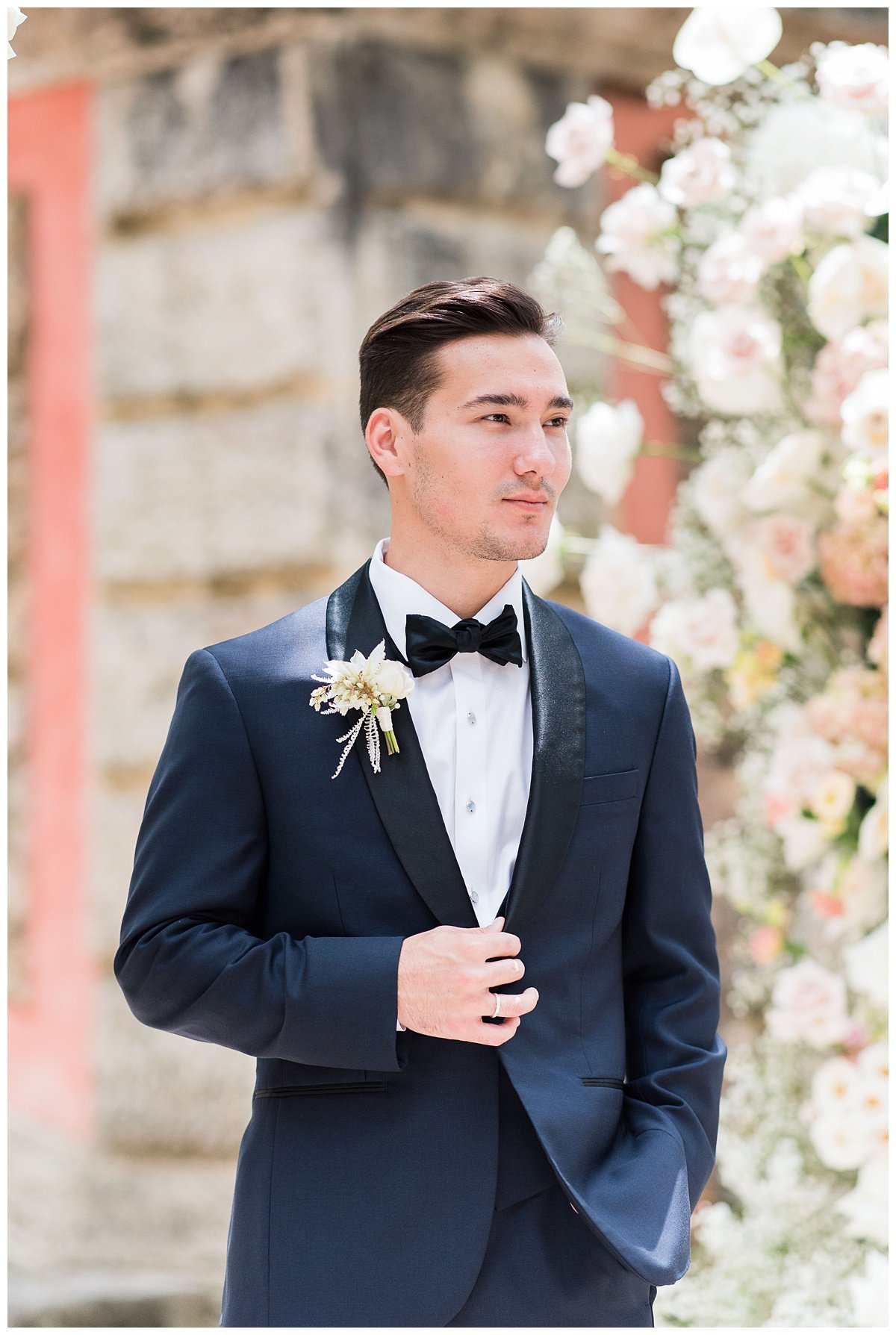 groom standing with hand on black tux during outdoor wedding ceremony