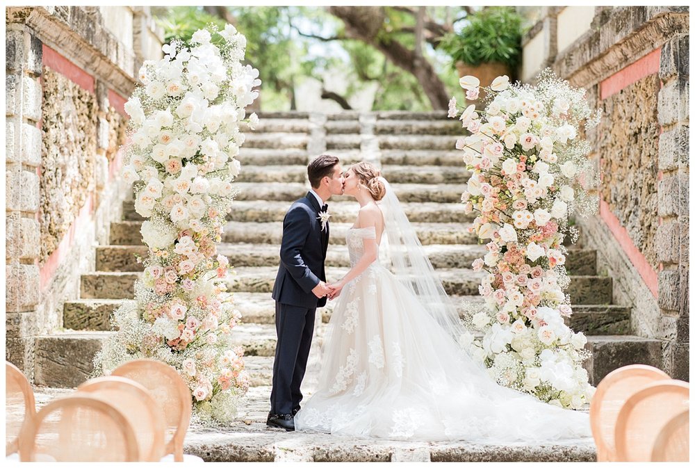 newlywed kissing on stairs at Miami Vizcaya Museum Wedding ceremony surrounded by floral column
