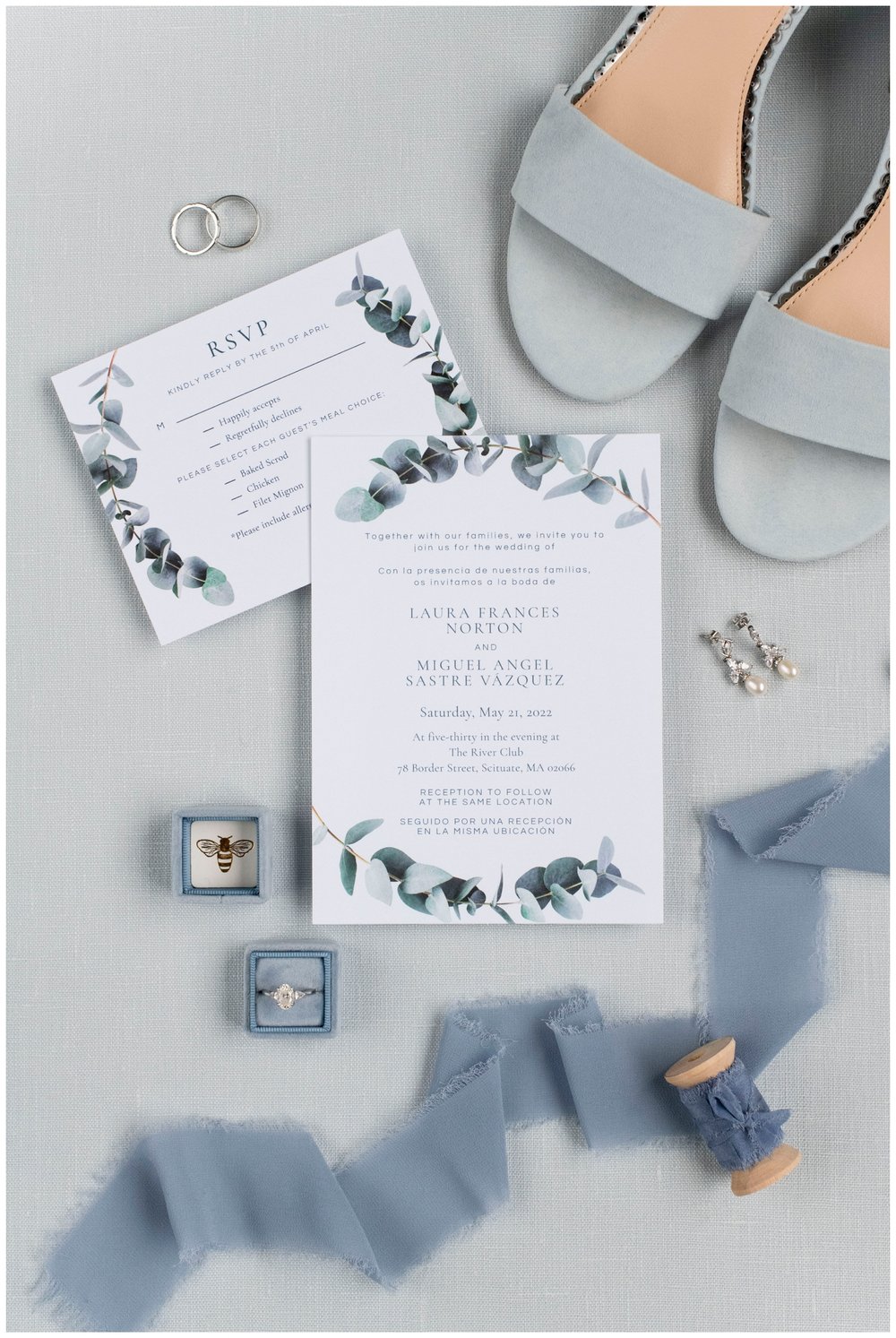 wedding flatlay with dusty blue heels, ribbon and ring on white invitation suite