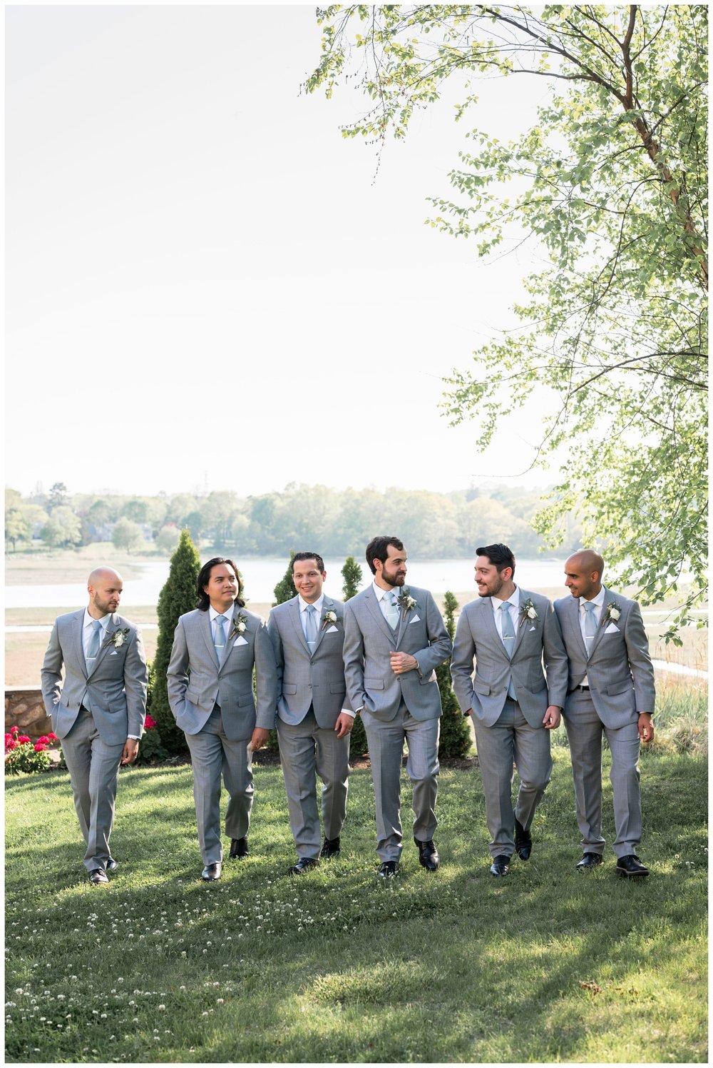 groom with groomsmen in gray suits walking under a tree