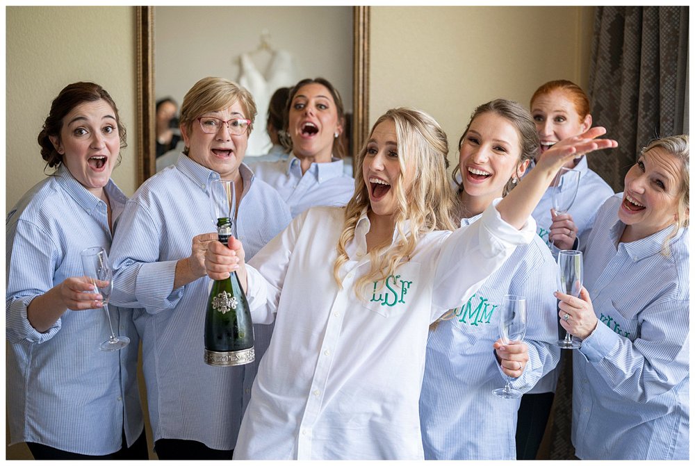 bride with bridesmaids popping bottle of champagne