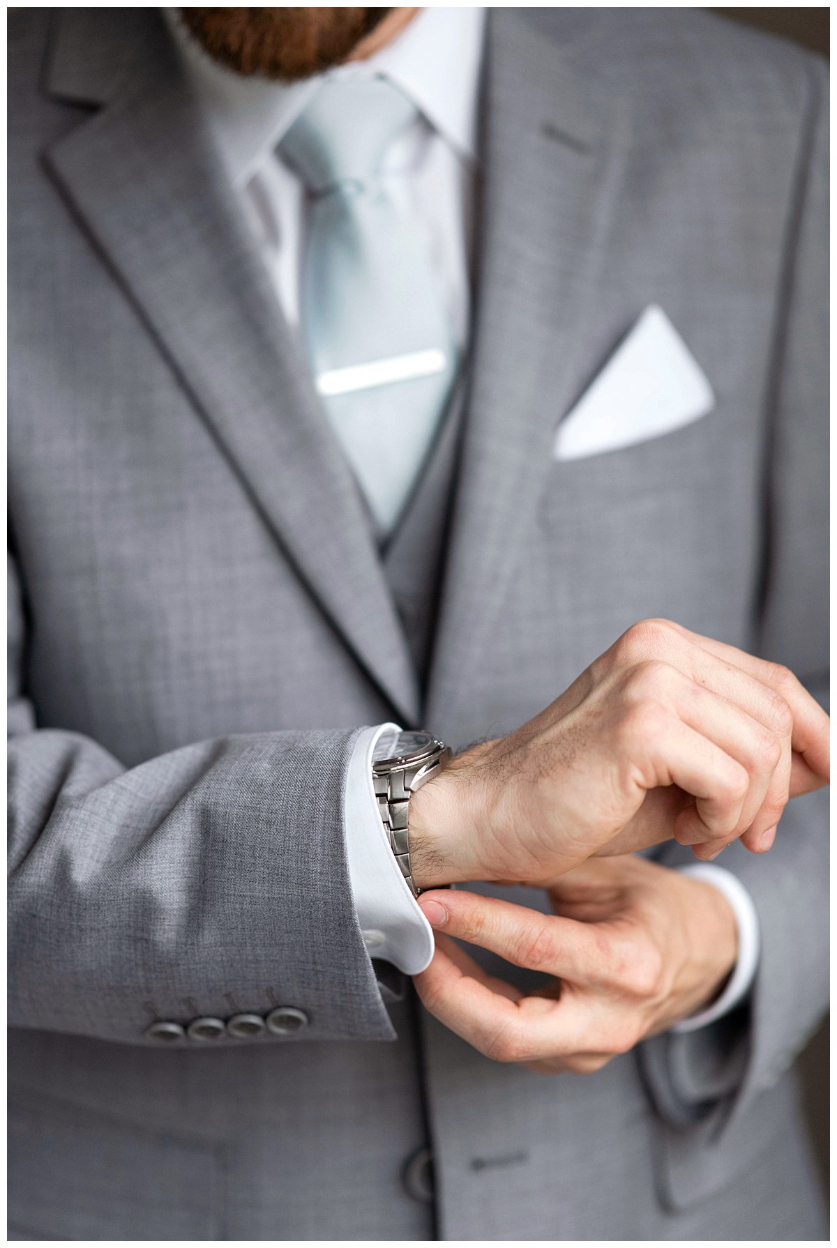 groom in gray suit fastening watch detail shot