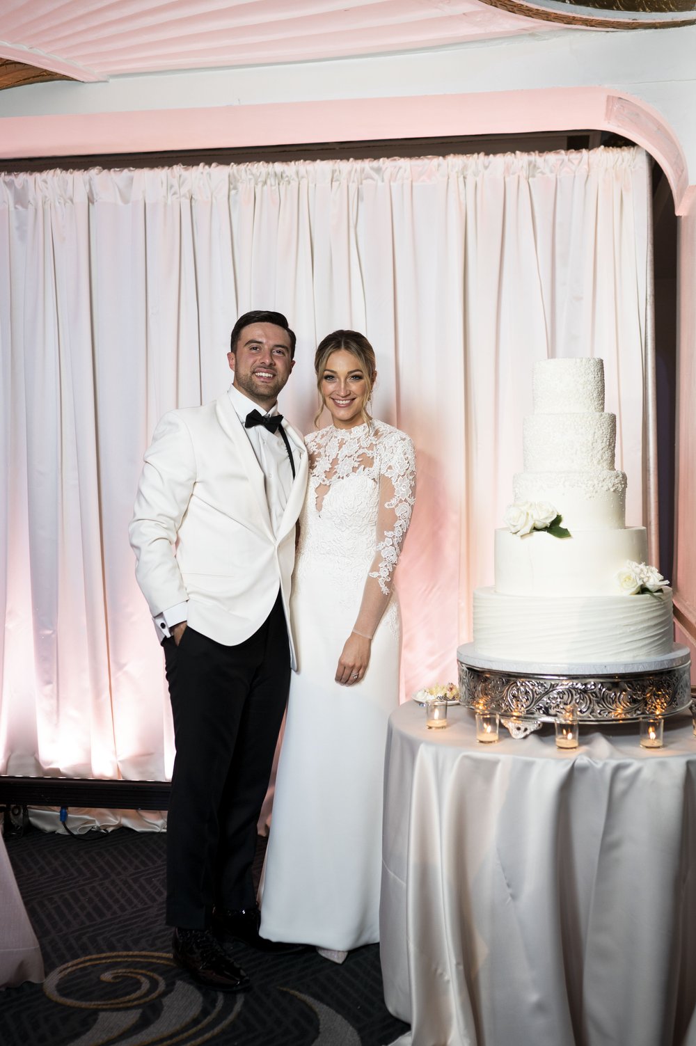 bride and groom smiling next to wedding cake