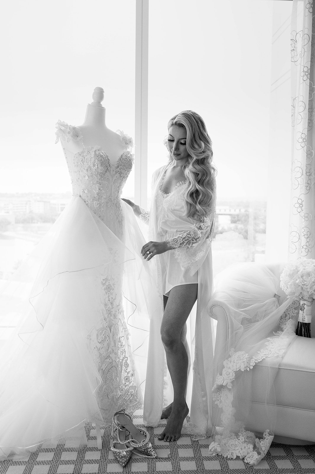 bride standing next to her wedding dress as she is holding the dress