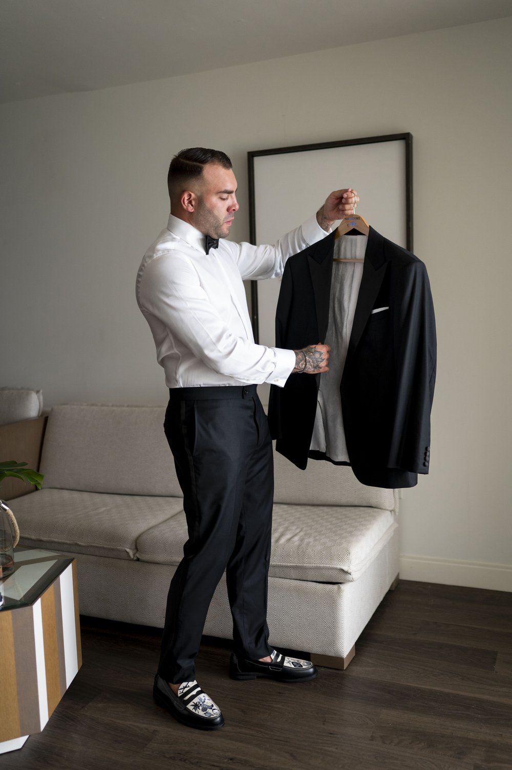 groom holds hanger with tuxedo jacket