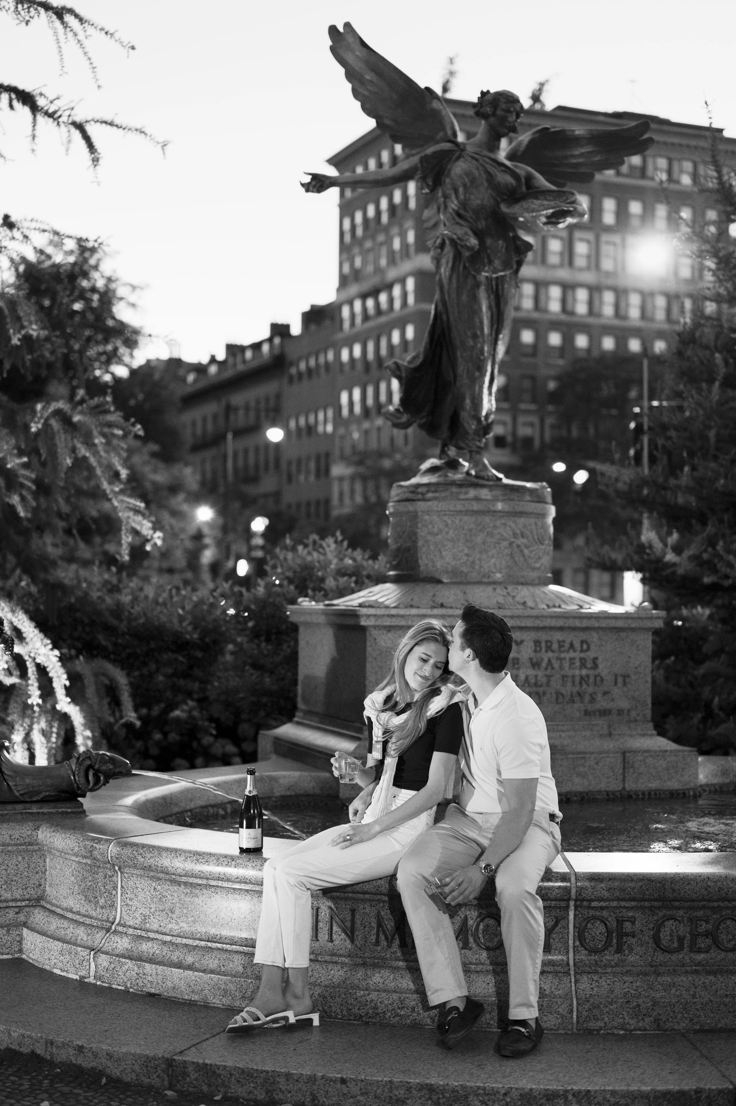 Cathryn and Brendan sitting by a fountain during their sunset engagement session at boston public garden
