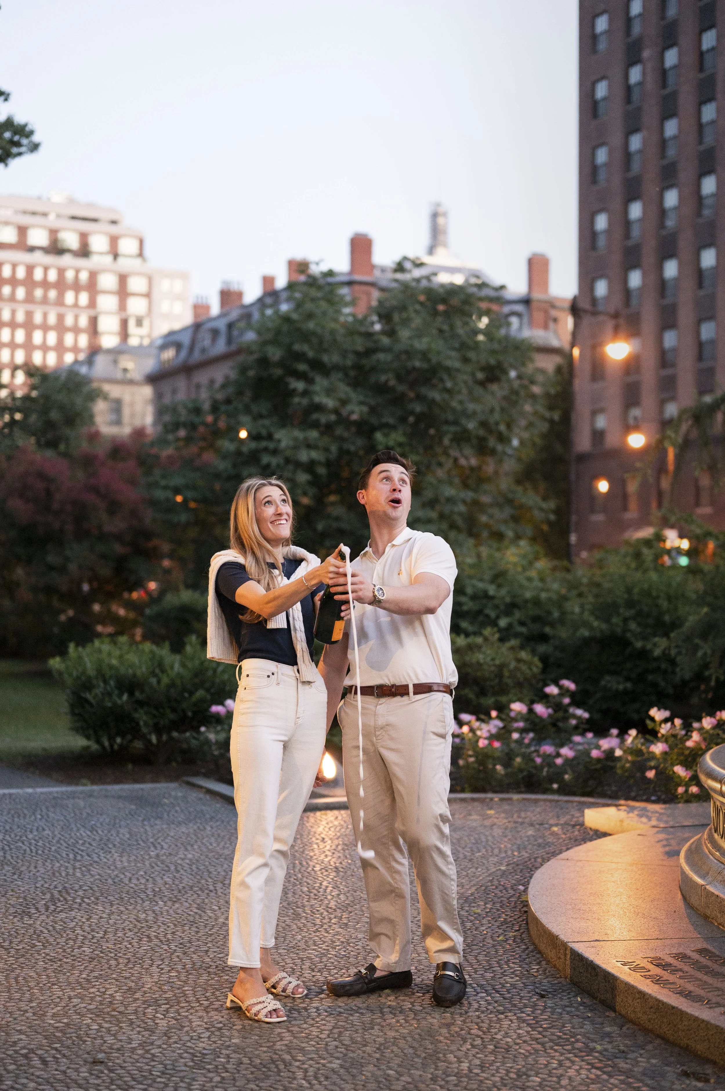 Cathryn and Brendan opening a champagne bottle during their sunset engagement session at boston public garden
