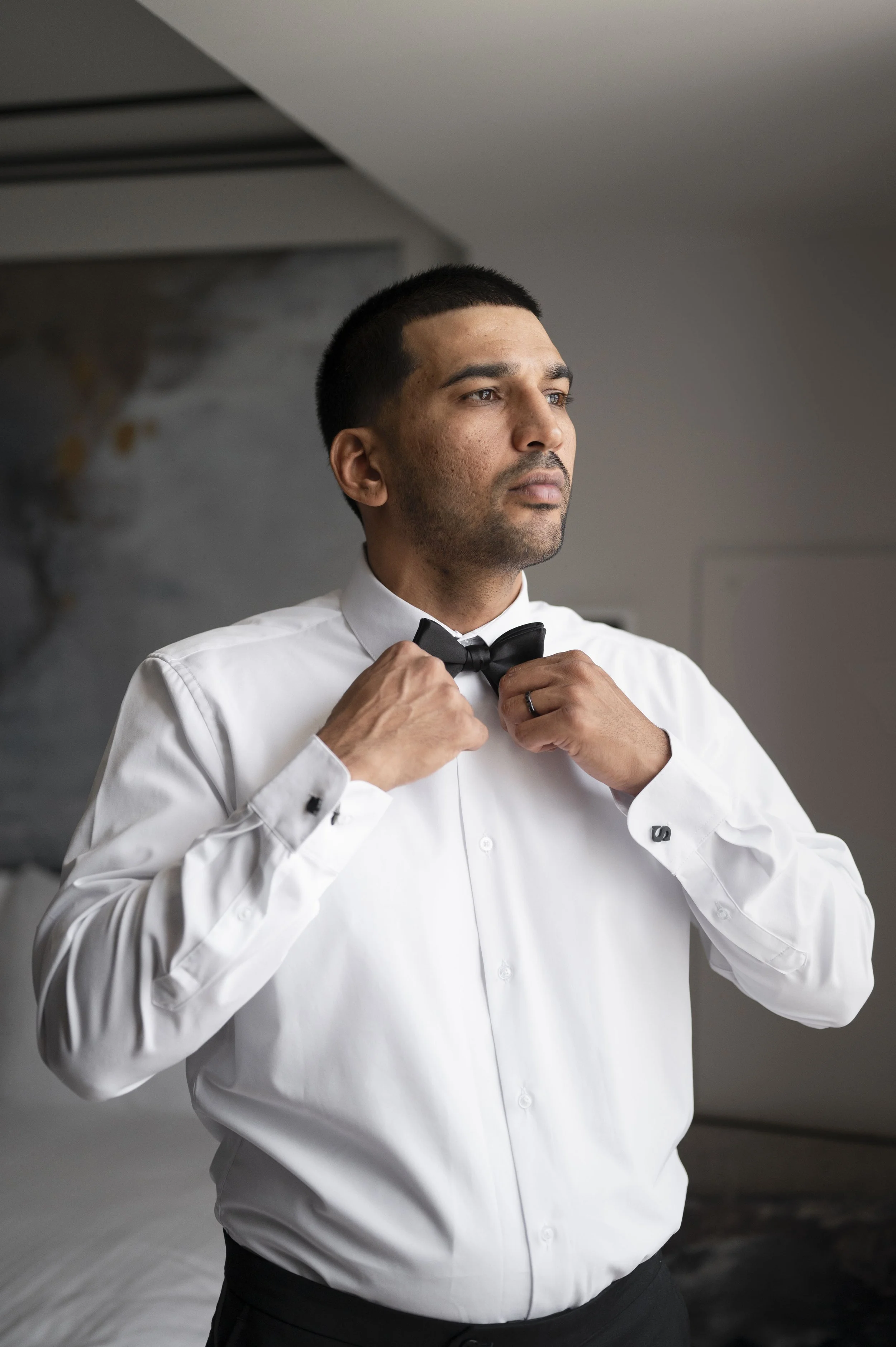 groom putting on his bow tie at the getting ready suite in the Loews hotel miami beach