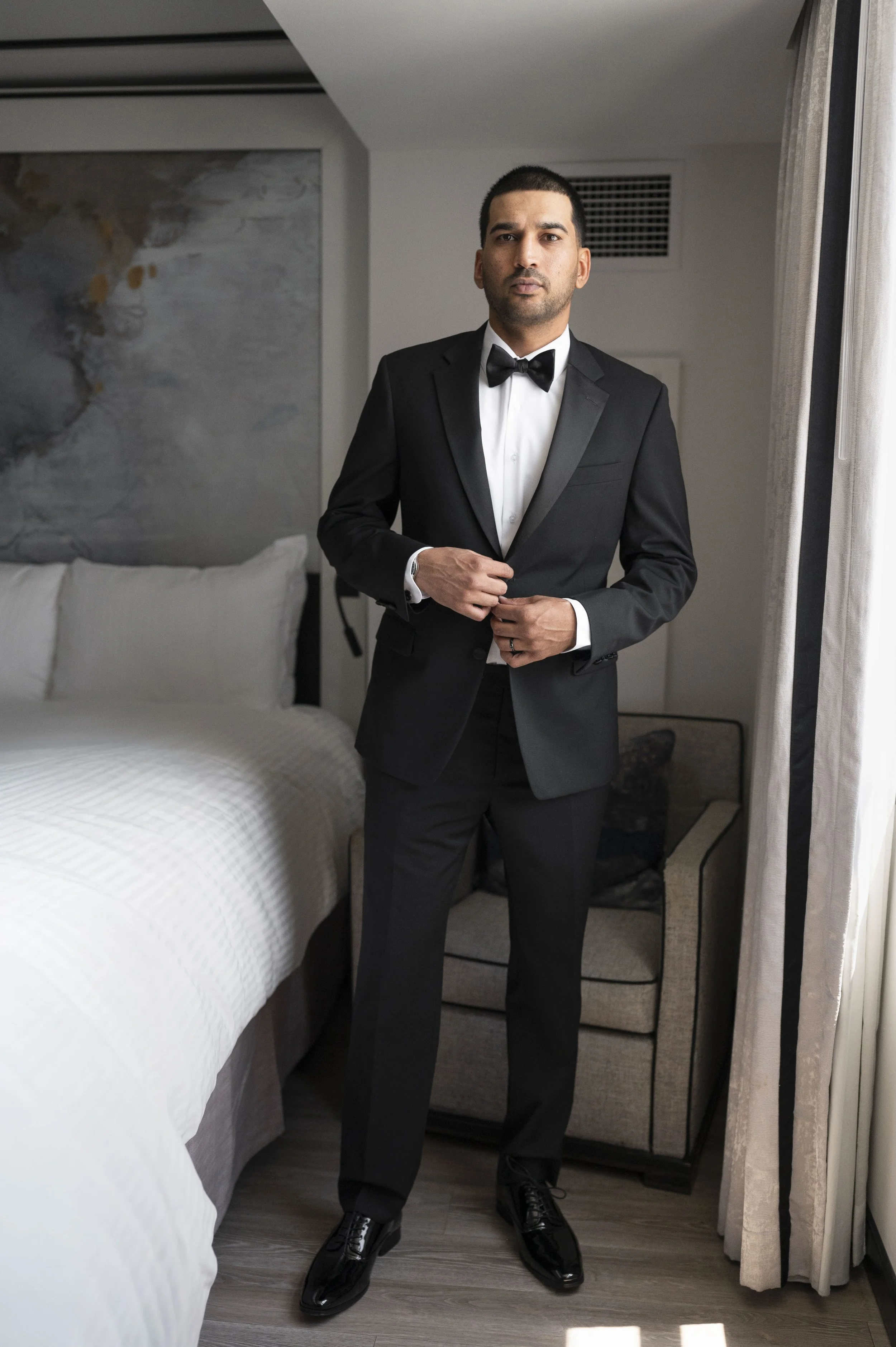 Groom standing in front of the camera looking at a mirror as he bottoms up his jacket at Loews hotel miami beach