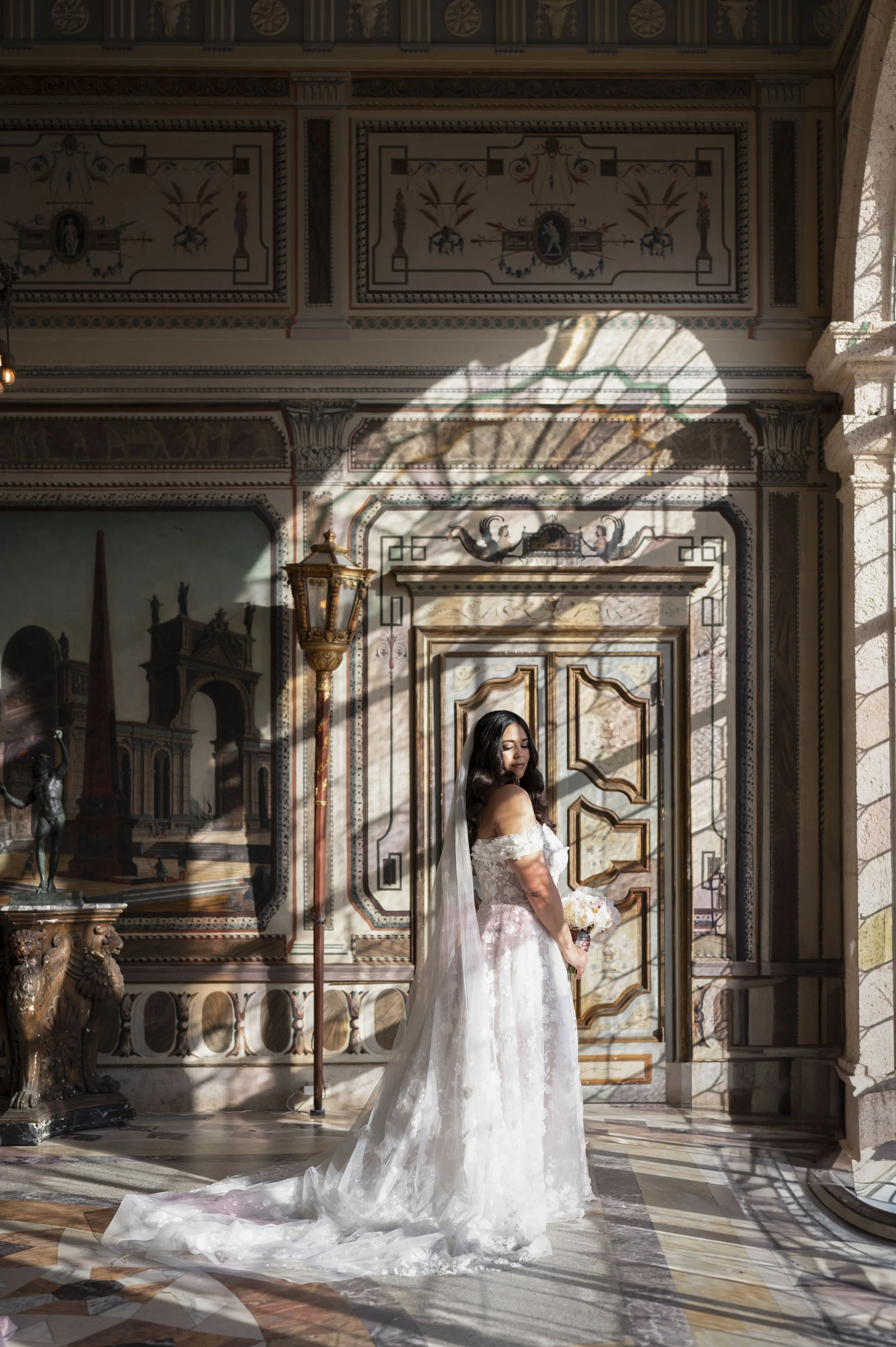 bride standing in front of a window which creates highlights and shadows on brides face at the vizcaya museum in miami