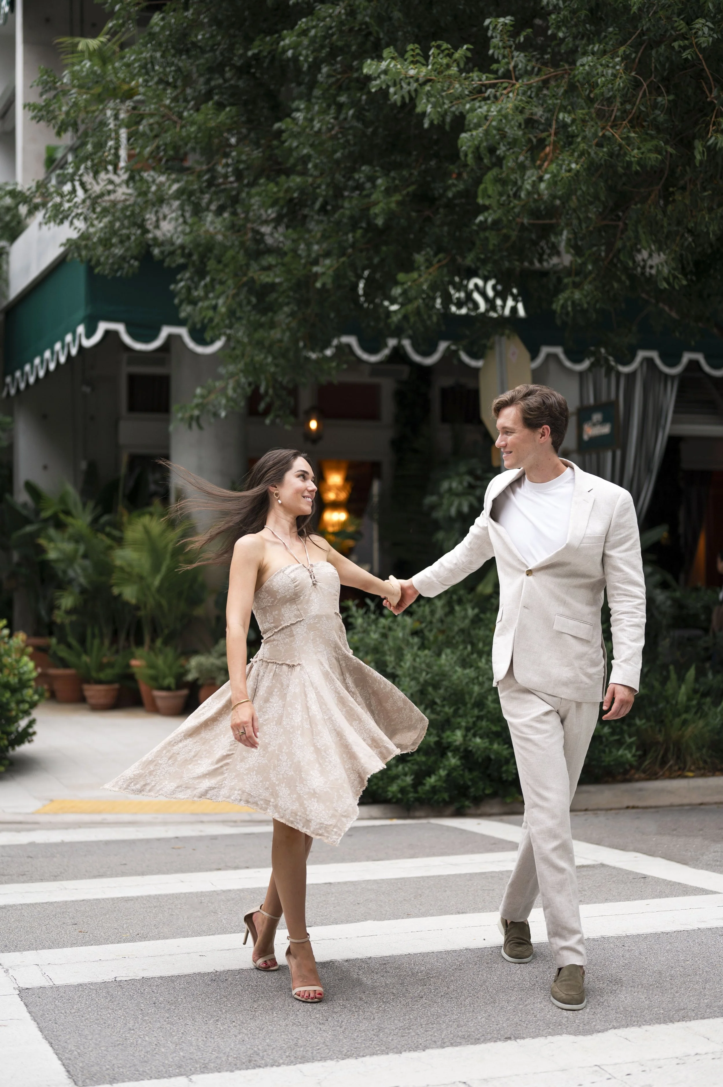 Rachel and Travis walking and spinning in front of contessa restaurant at Miami design district during their engagement session.
