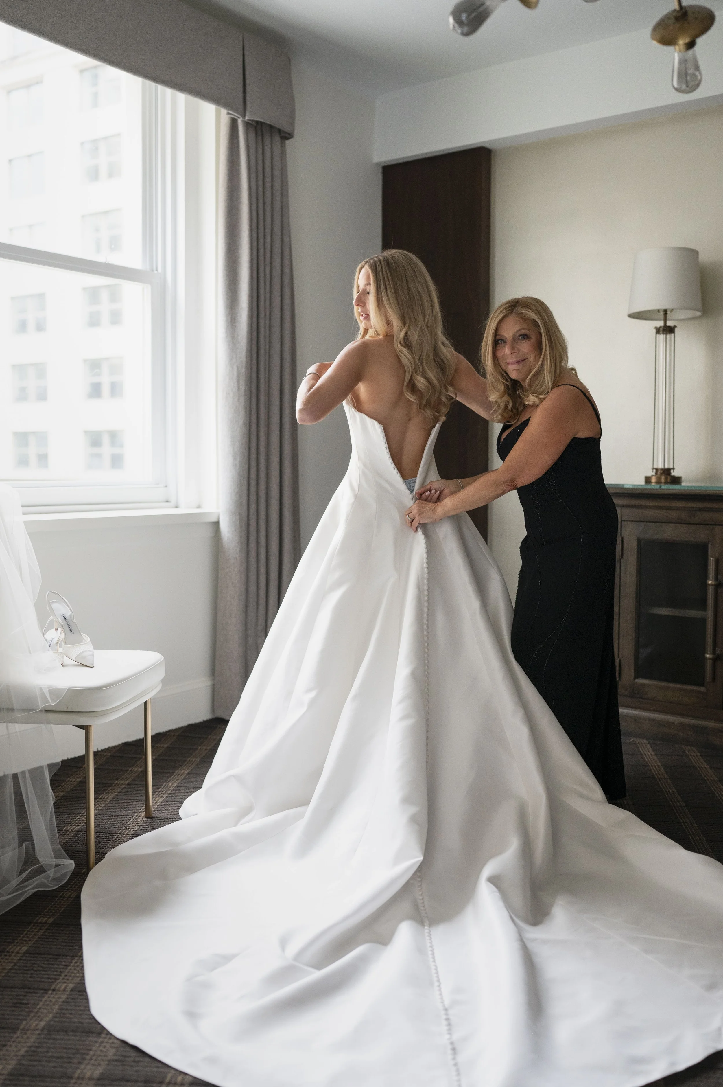 bride putting her dress on with the help of her mom her wedding day 