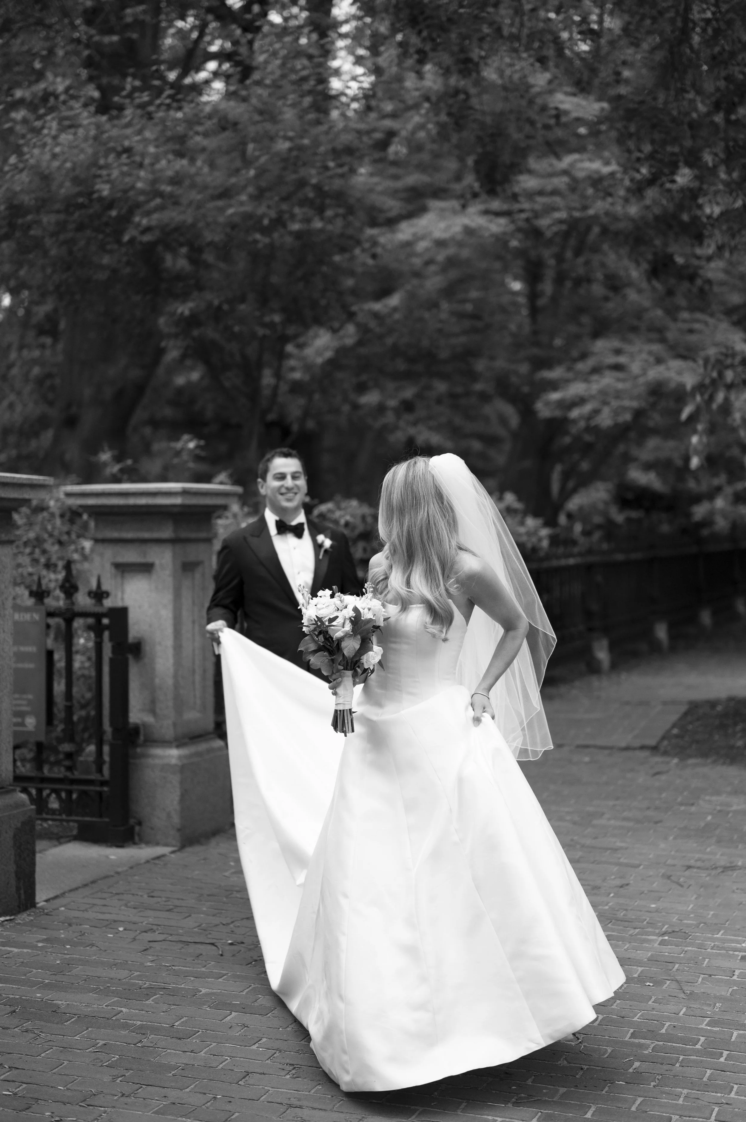 groom holds brides dress as they walk together