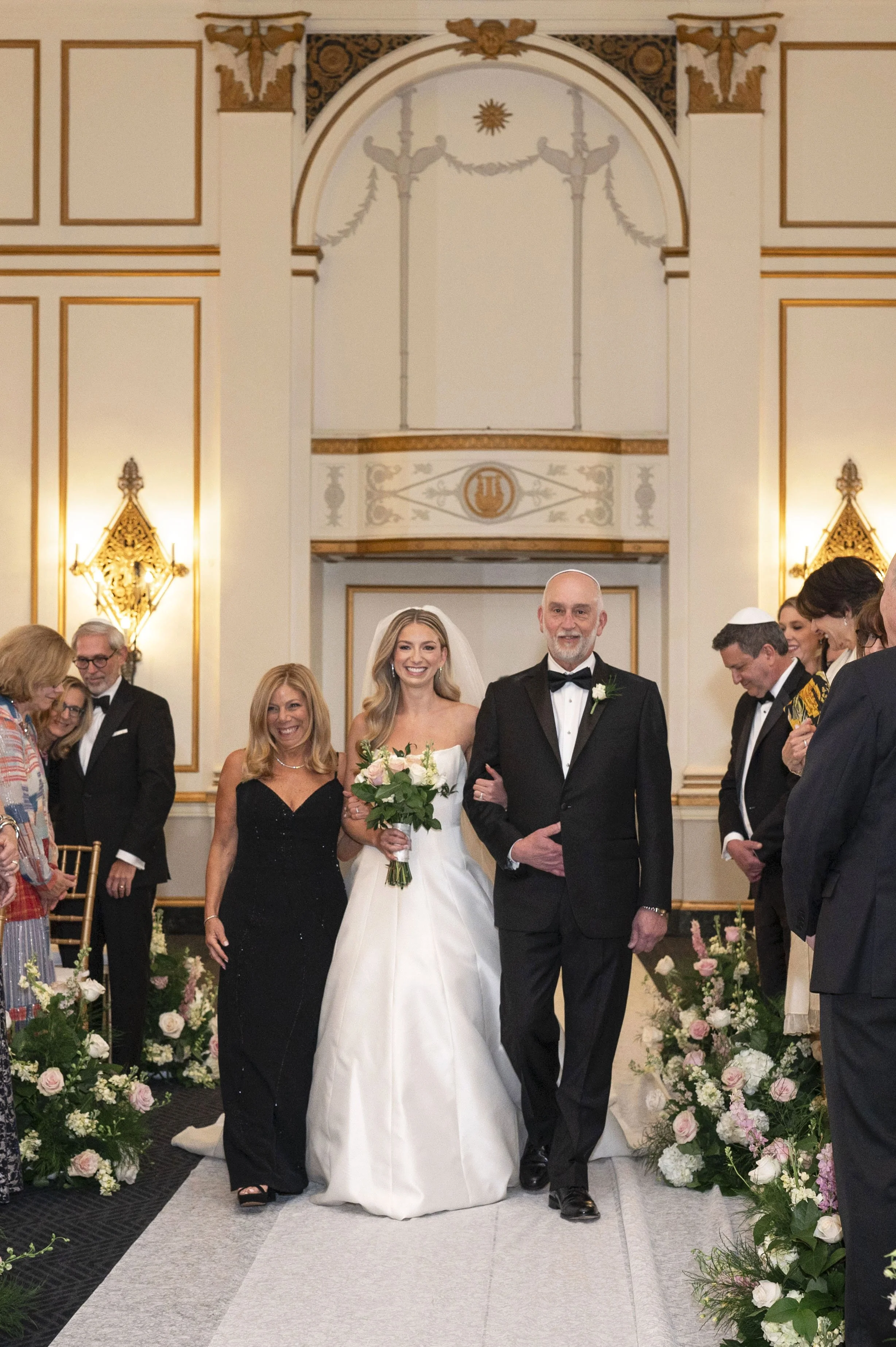 bride walking down the isle with her mother and father during her jewish ceremony at the boston park plaza