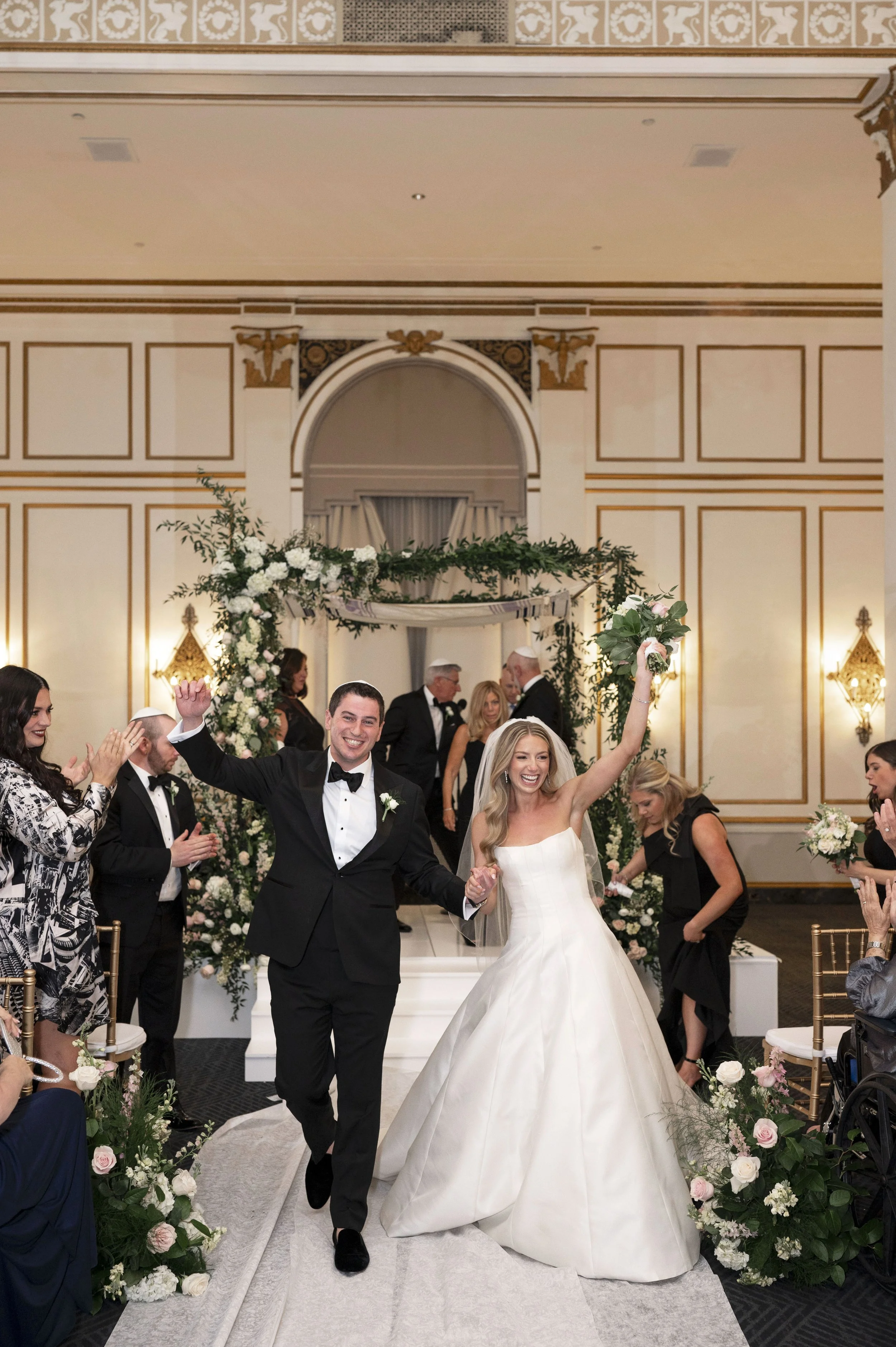 bride and groom walking as husand and wife holding hands and cheering at the park plaza hotel during their jewish ceremony