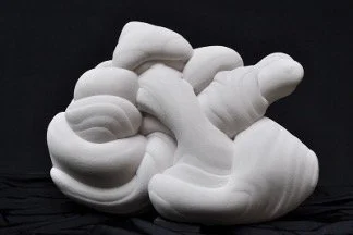 An abstract, white sandstone sculpture featuring interlocking, bulbous forms and a textured, swirled surface set against a dark black background.