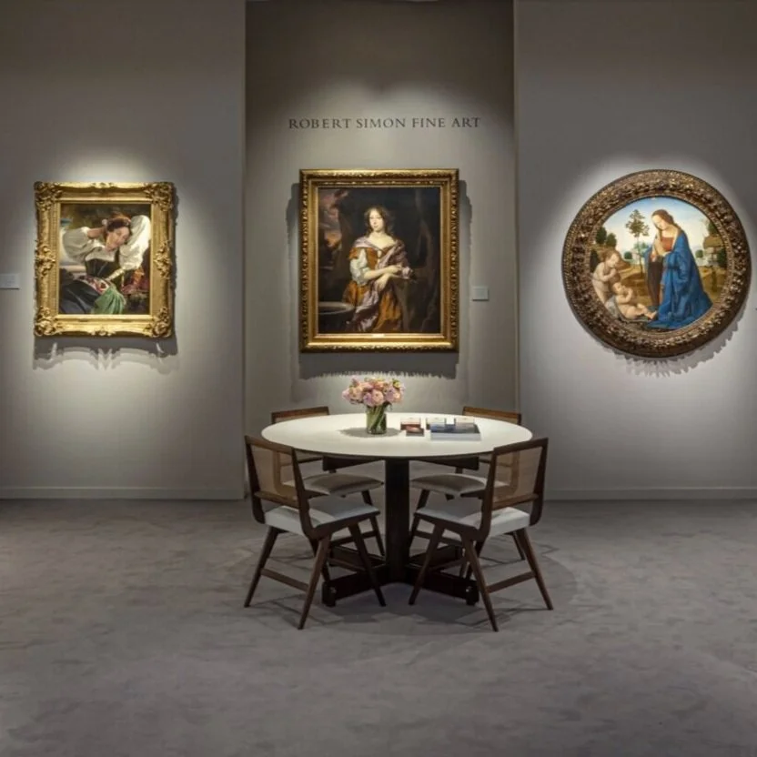 Front view of booth. Round table with flowers. Three artworks on wall.