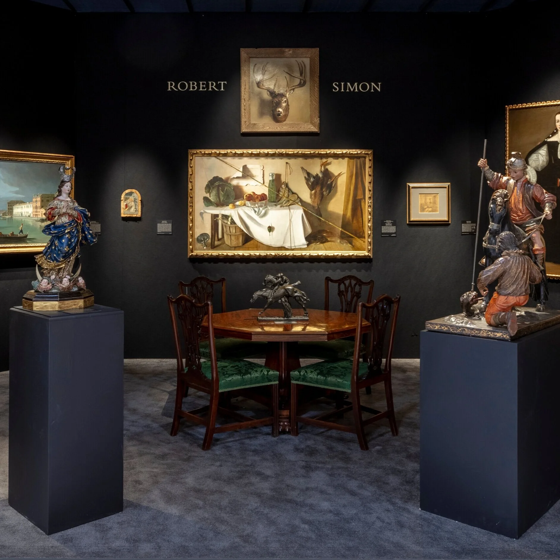 Front view of booth. Artworks on walls, antique table in the middle.