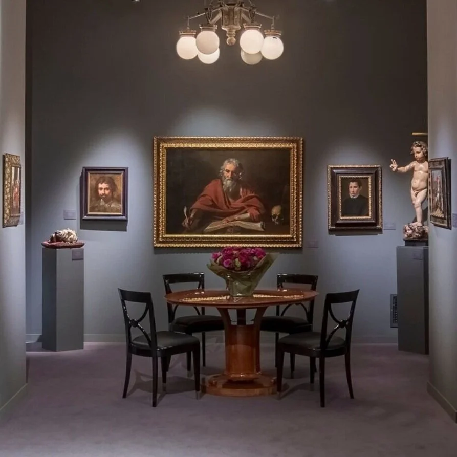interior of booth. Two pedestals, a table with flowers, and a painting of a man in red above.