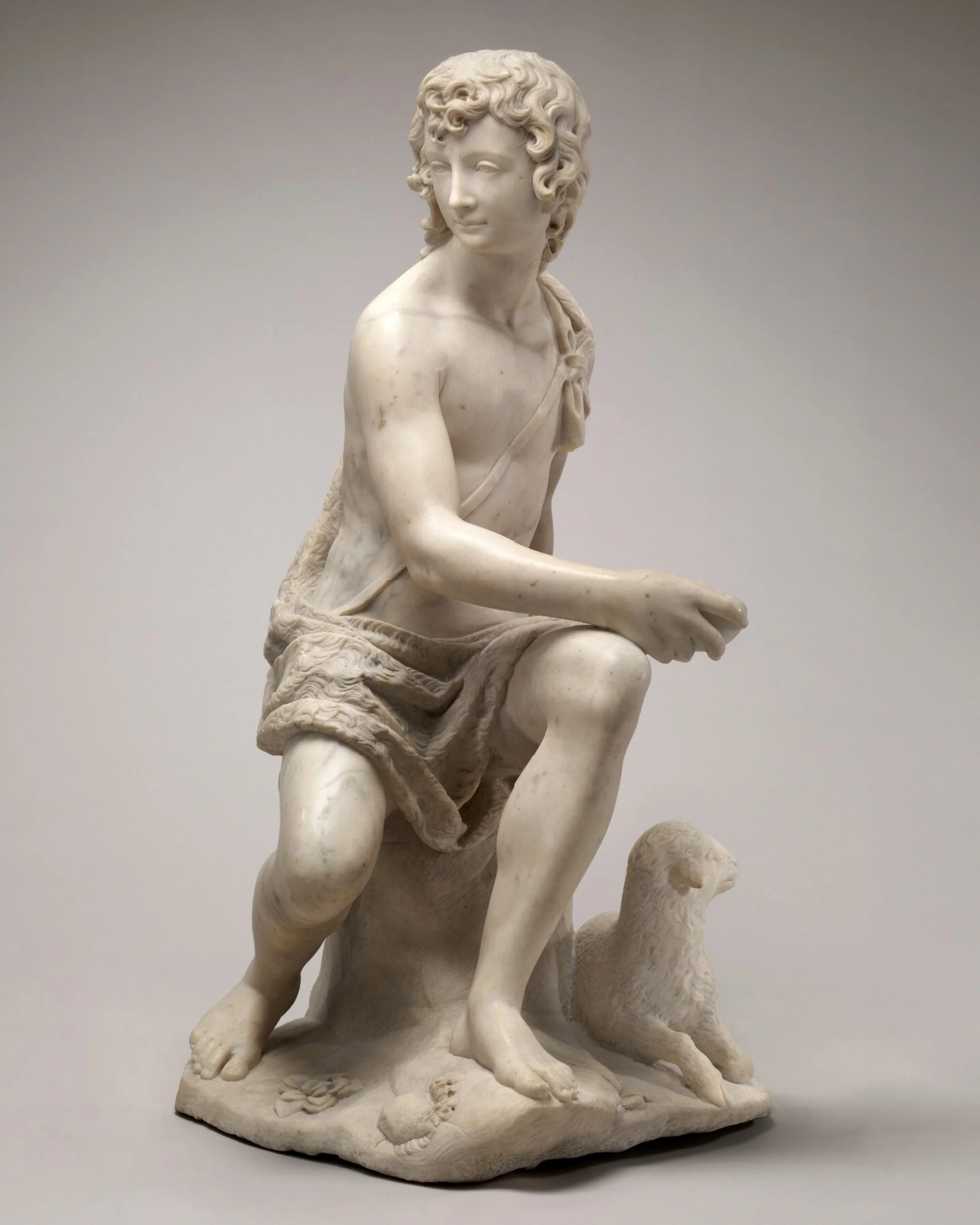 A marble statue of a man seated on a stump. Lamb at his feet.