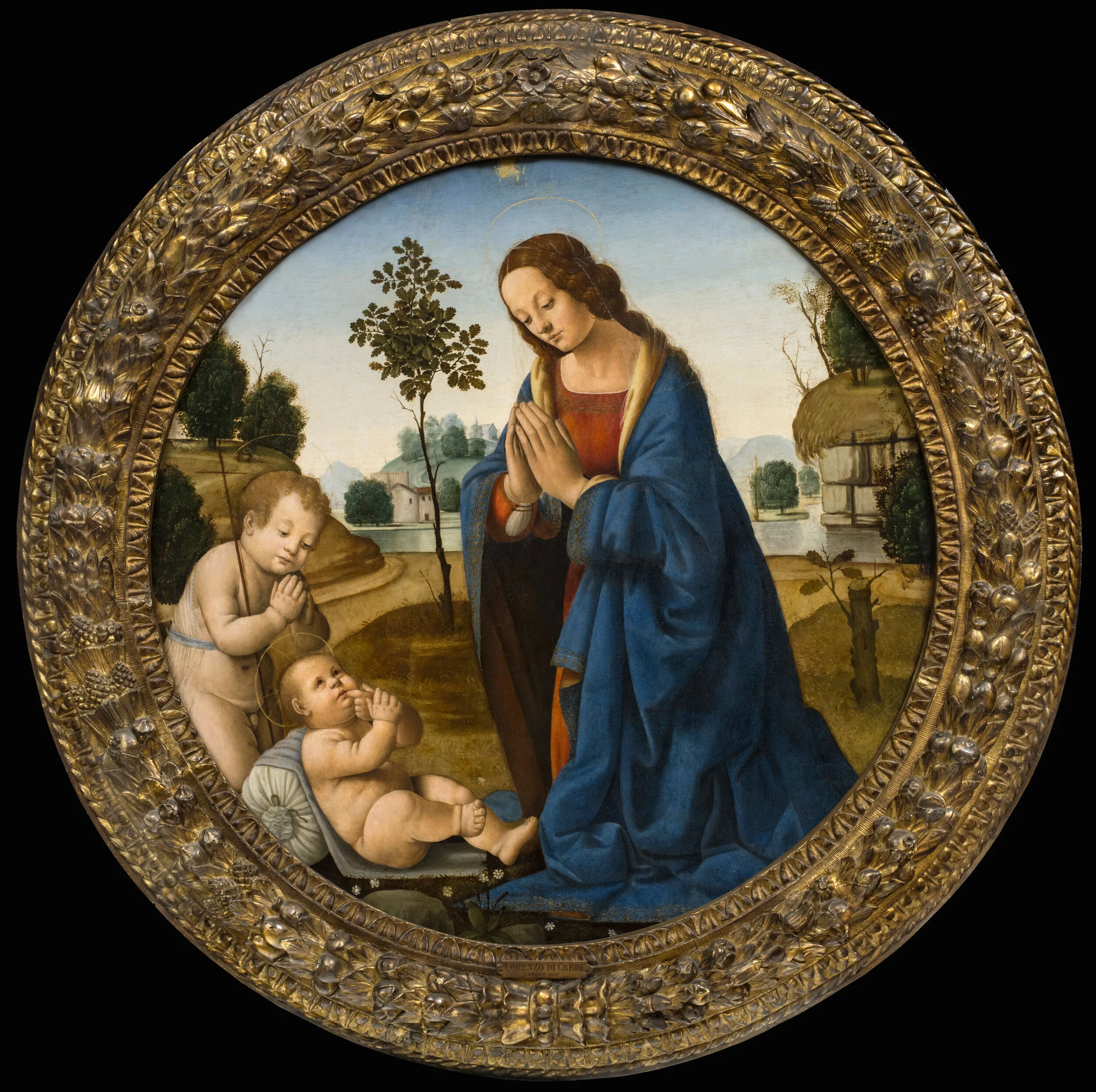 A round artwork in a gilded frame. Mary kneels and prays over Jesus and John.