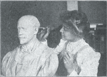 Woman with short hair holding compass to measure ear of a sculpture of a bald man