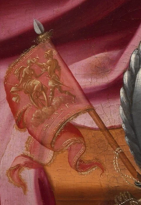 Detail of red flag embroidered in gold, depicting a winged female figure on wheel and an armored man