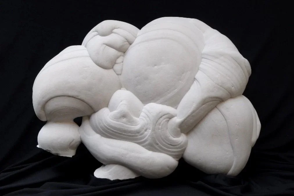 Reverse side of an abstract, white sandstone sculpture featuring rounded, bulbous forms and a broad, asymmetrical silhouette set against a solid black background.