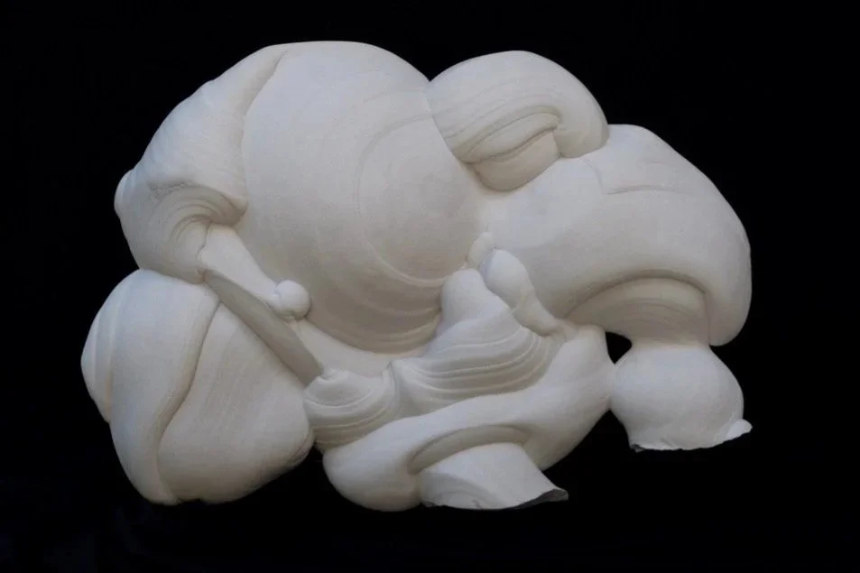 An abstract, white sandstone sculpture featuring rounded, bulbous forms and a broad, asymmetrical silhouette set against a solid black background.