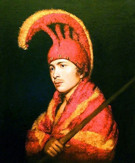 Portrait of an indigenous man in a red and orange headdress and mantle.