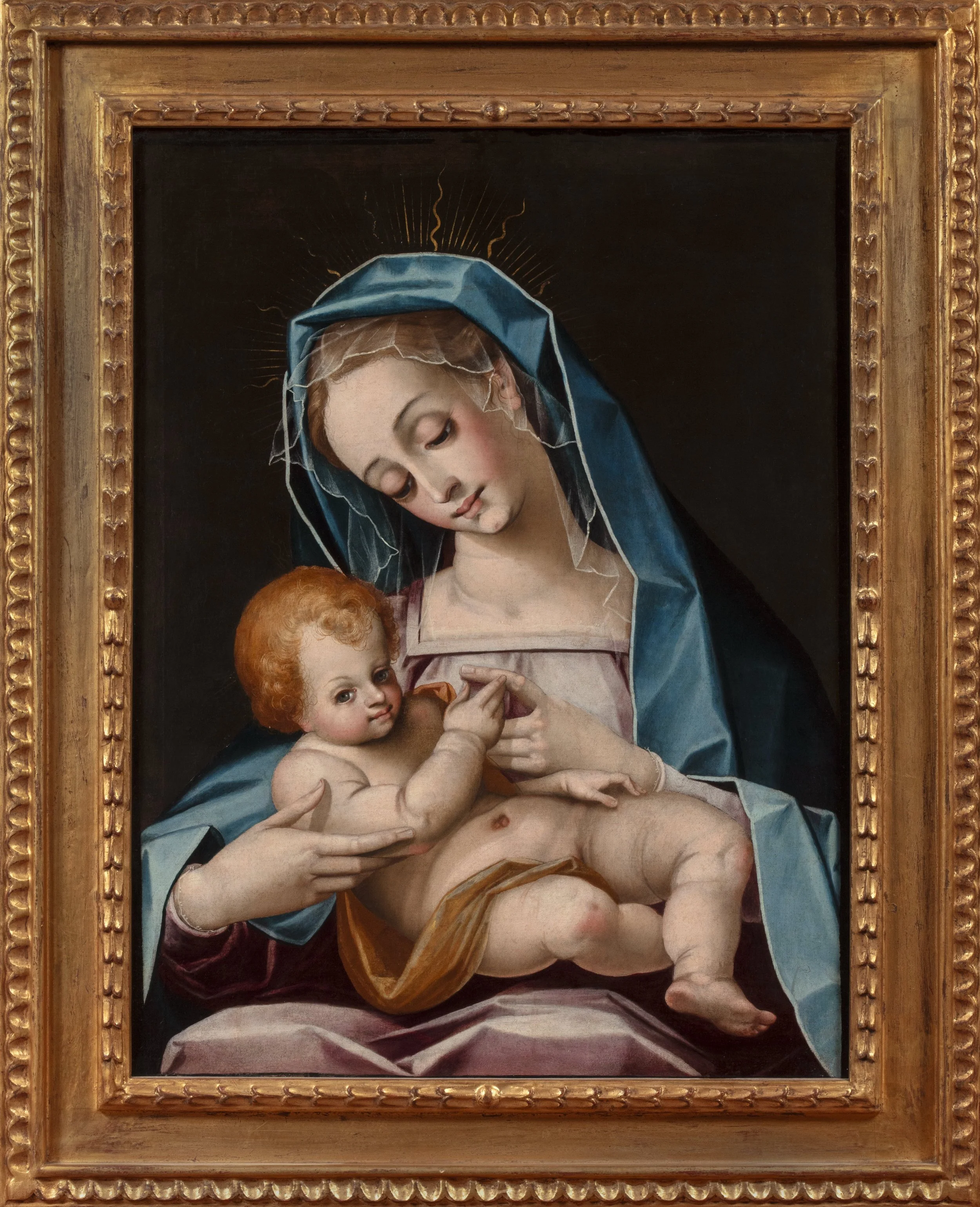 A seated young woman with blue and pink cloak holds a nude baby against a black background.