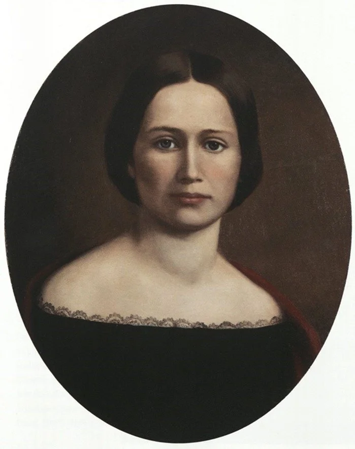 Oval portrait of woman with short hair wearing black dress against plain background