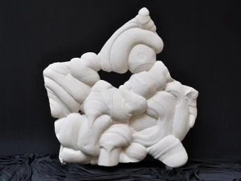 Reverse side of an abstract, white sandstone sculpture with a rough triangular silhouette set against a black background