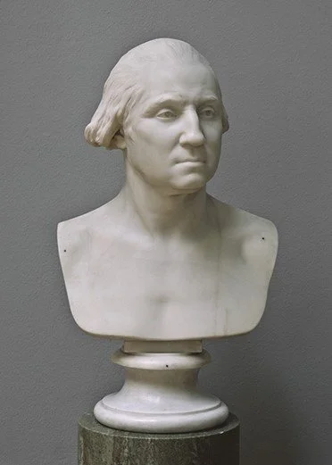 Sculpture of a bust of a man with long hair sitting on top of a column.