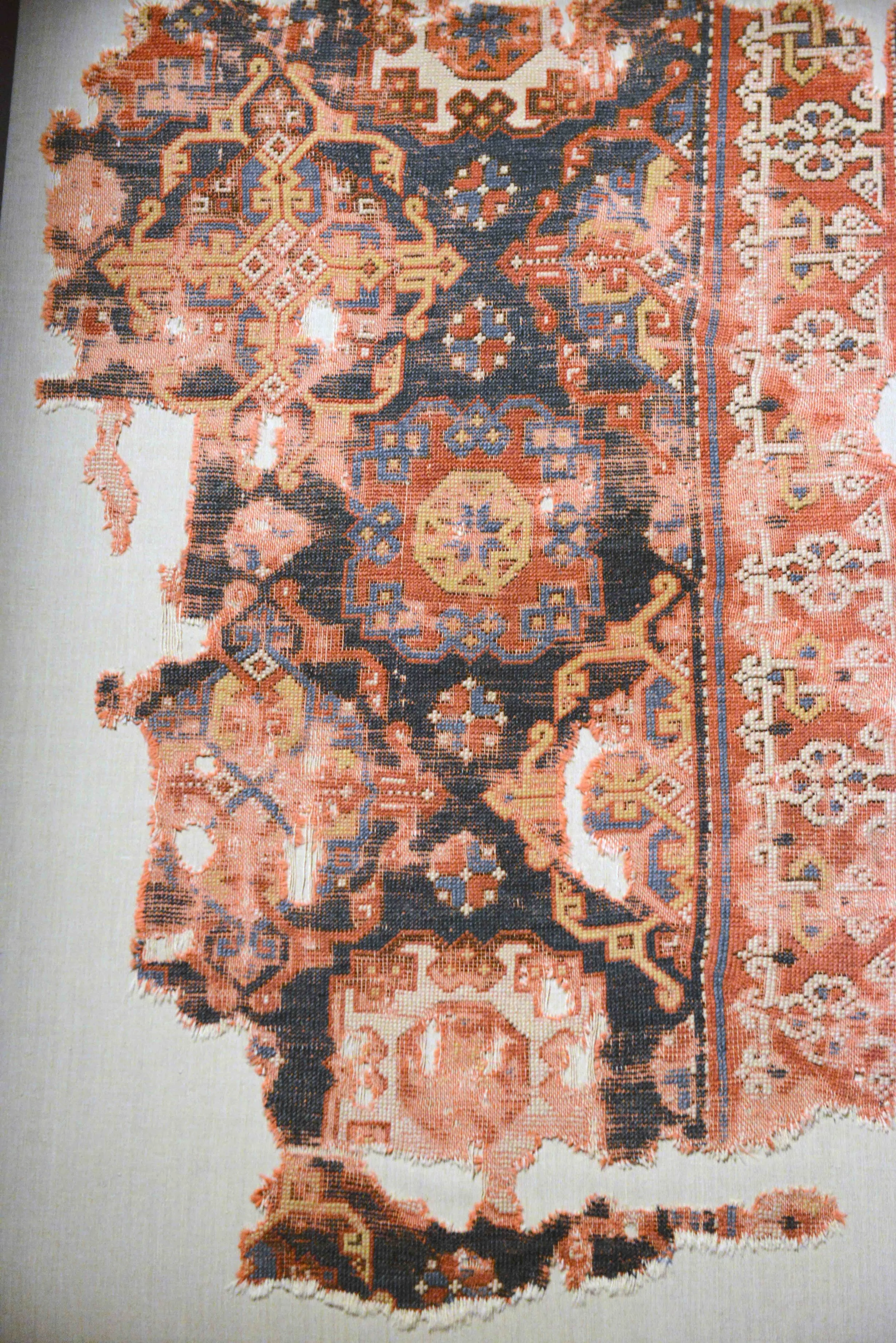 Partially destroyed antique rug with red ground and prominent blue, yellow, and white geometric desgins.