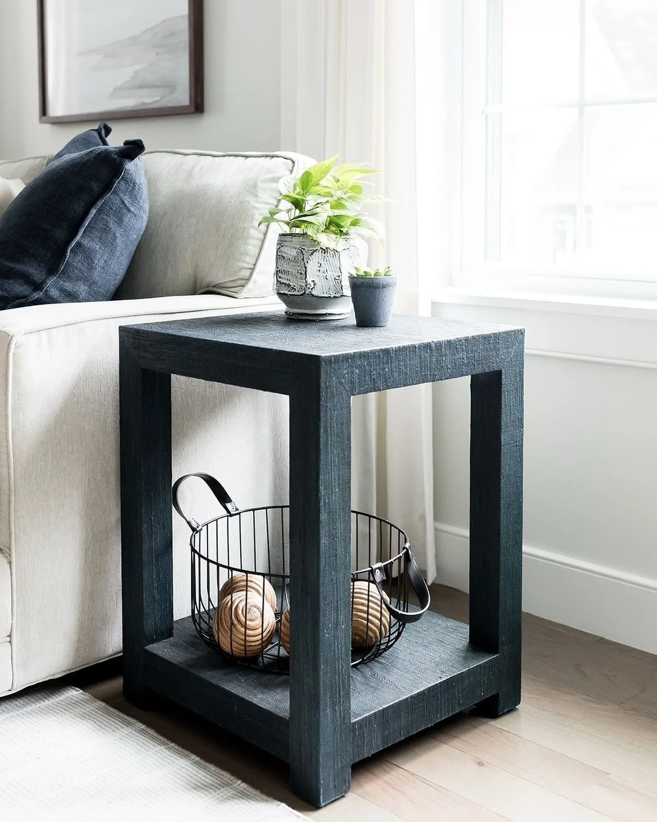 This navy blue side table has a lot going for it - color, texture (linen wrapped wood) and negative space (the open shelf is a wonderful balance to the darker color). The height is a perfect match to the arm of the sofa next to it and the color contr