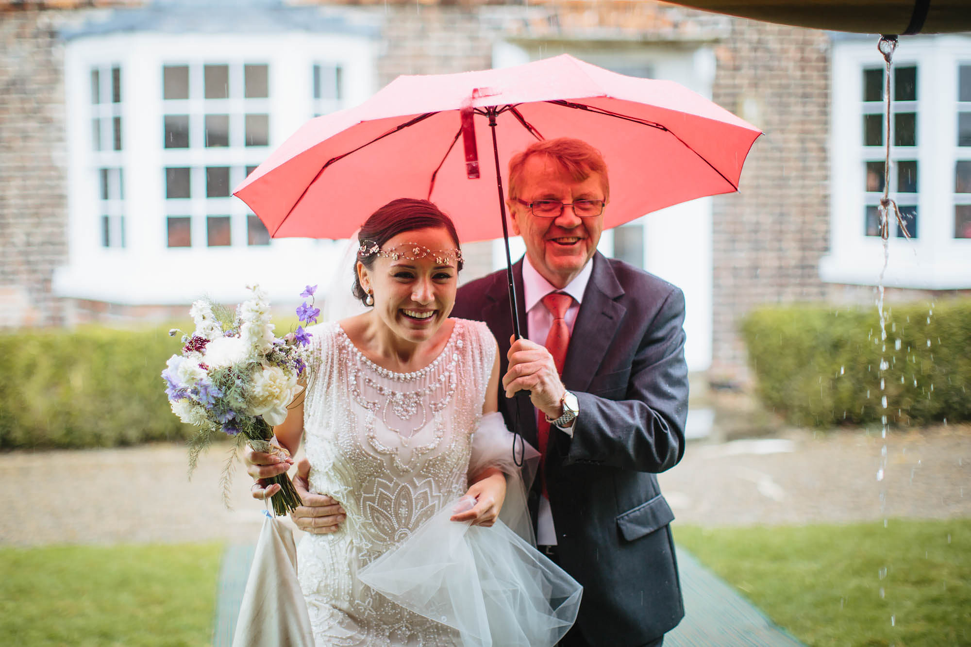 Bride and father under an umbrella in the rain