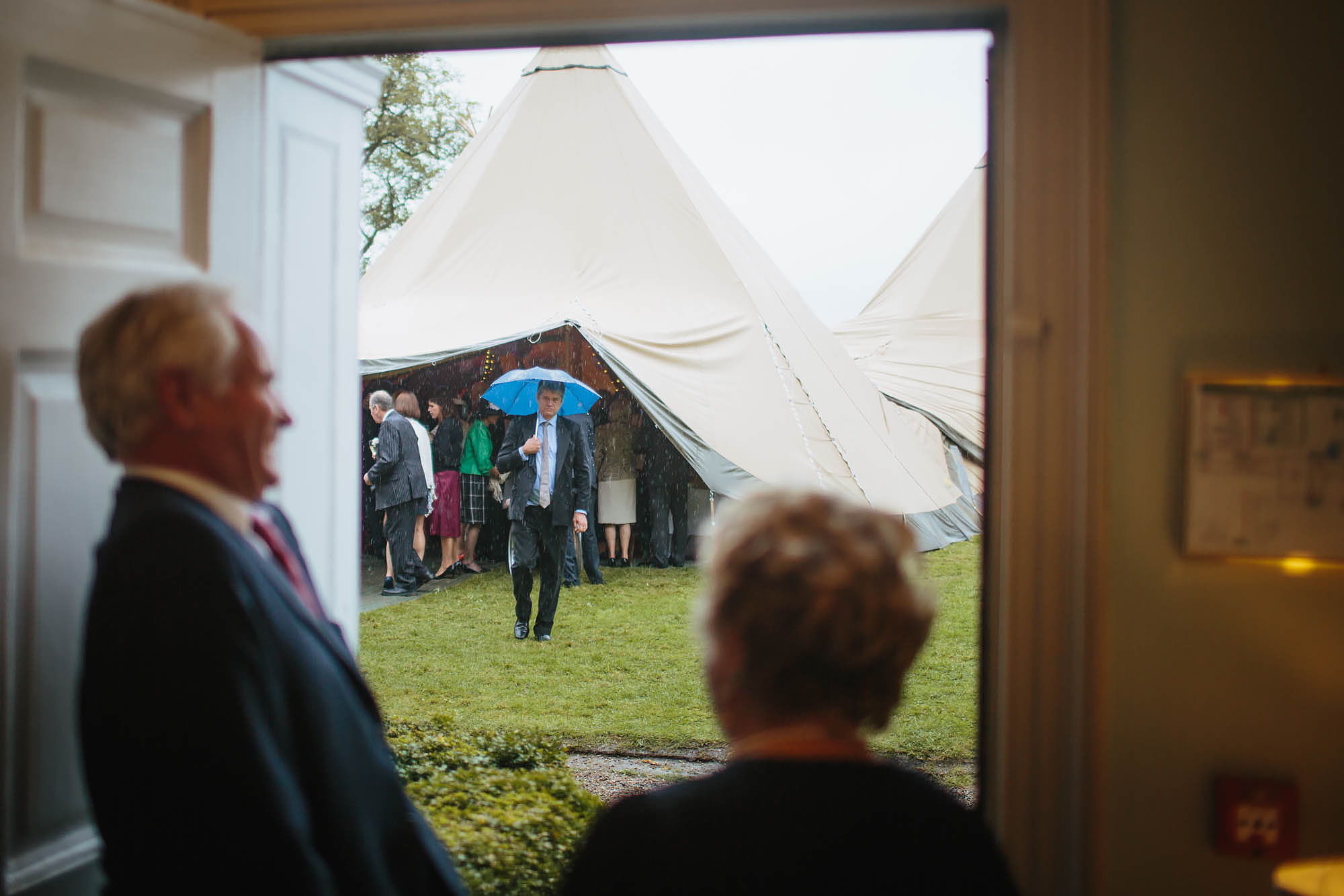 Guests laughing at a man with an umbrella at a wedding