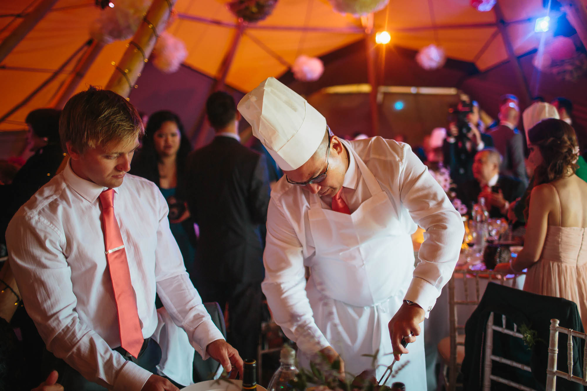 Guests carving meat at the table in a chefs hat at a tipi wedding